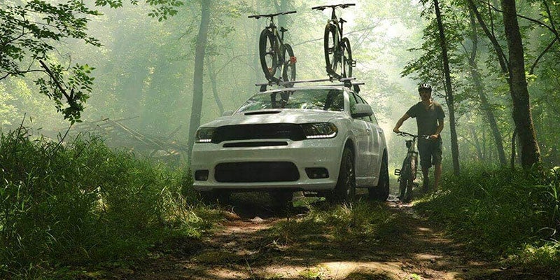a white 2020 dodge durango parked with bikes on the bike rack on top of the vehicle in the woods