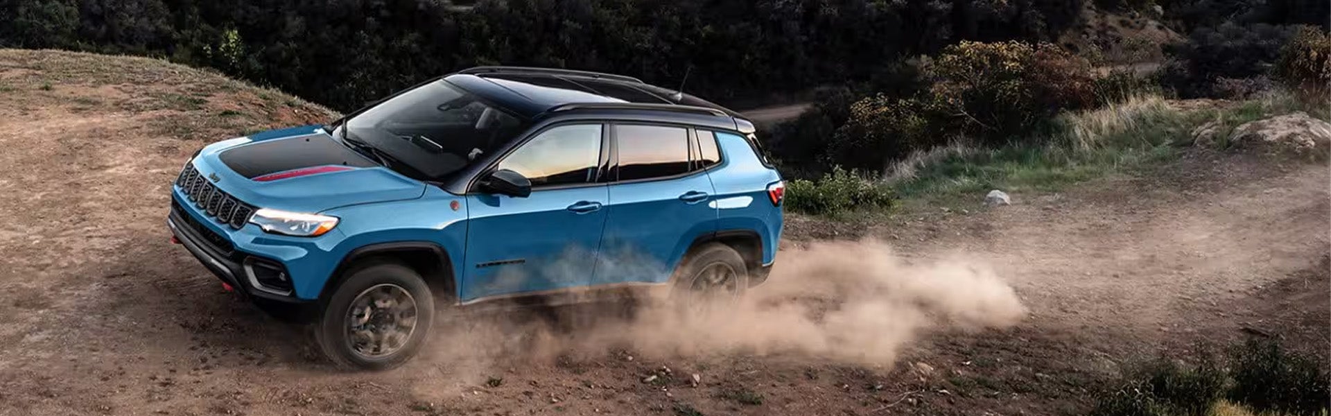 a blue 2025 jeep compass driving on a dirt road