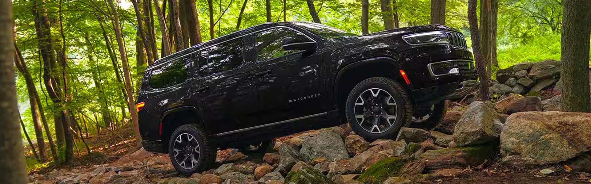 A black 2025 Jeep Grand Wagoneer sitting on some rocks in a forest.