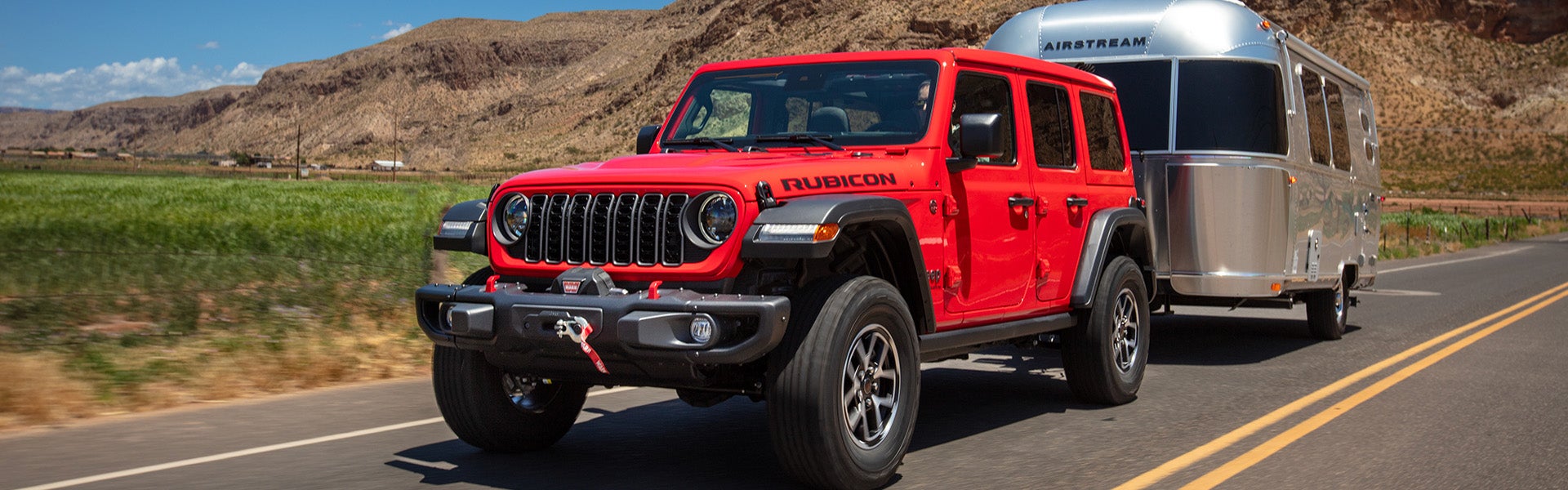 A red jeep pulling a trailer on the road.