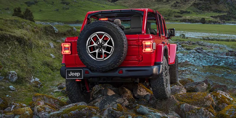 A red jeep driving over some rocks.