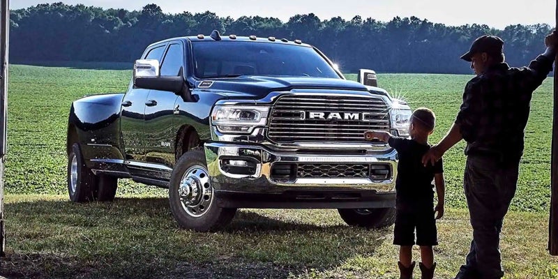 a man and boy standing in front of a ram 3500 in an open field