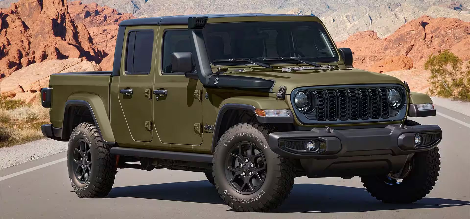 a green jeep gladiator parked on a paved road near the dessert