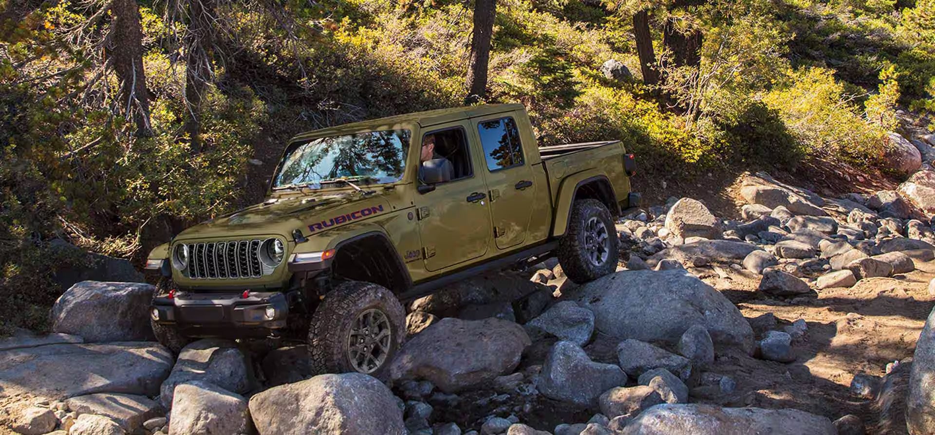 a jeep gladiator driving over larges rocks in a creek bed