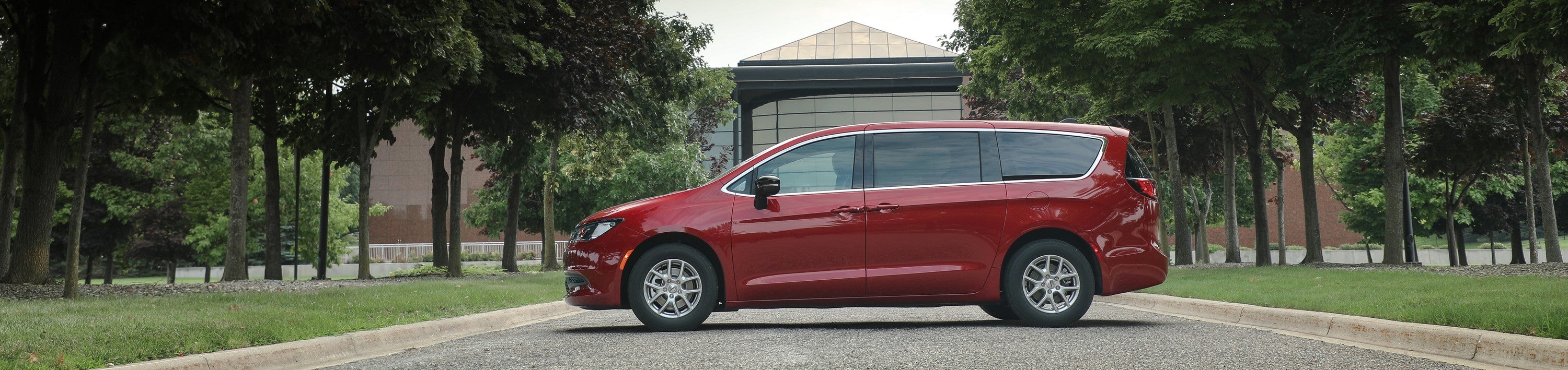 a red minivan parked next to a large building with large glass windows.