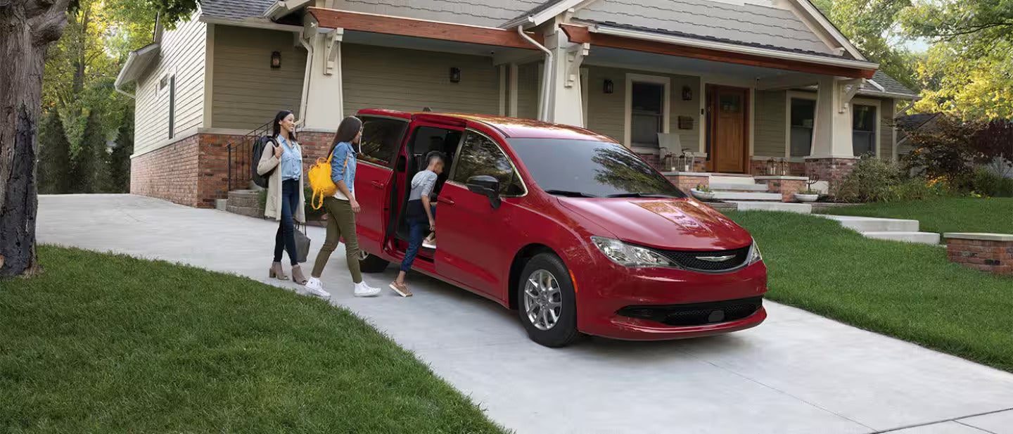 a family getting into a red chrysler voyager parked in a driveway