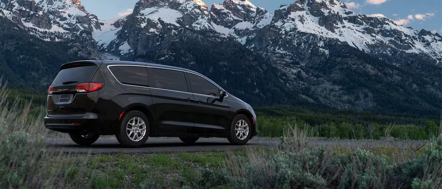 a black chrysler voyager parked in the grass overlooking snow capped mountains at night.