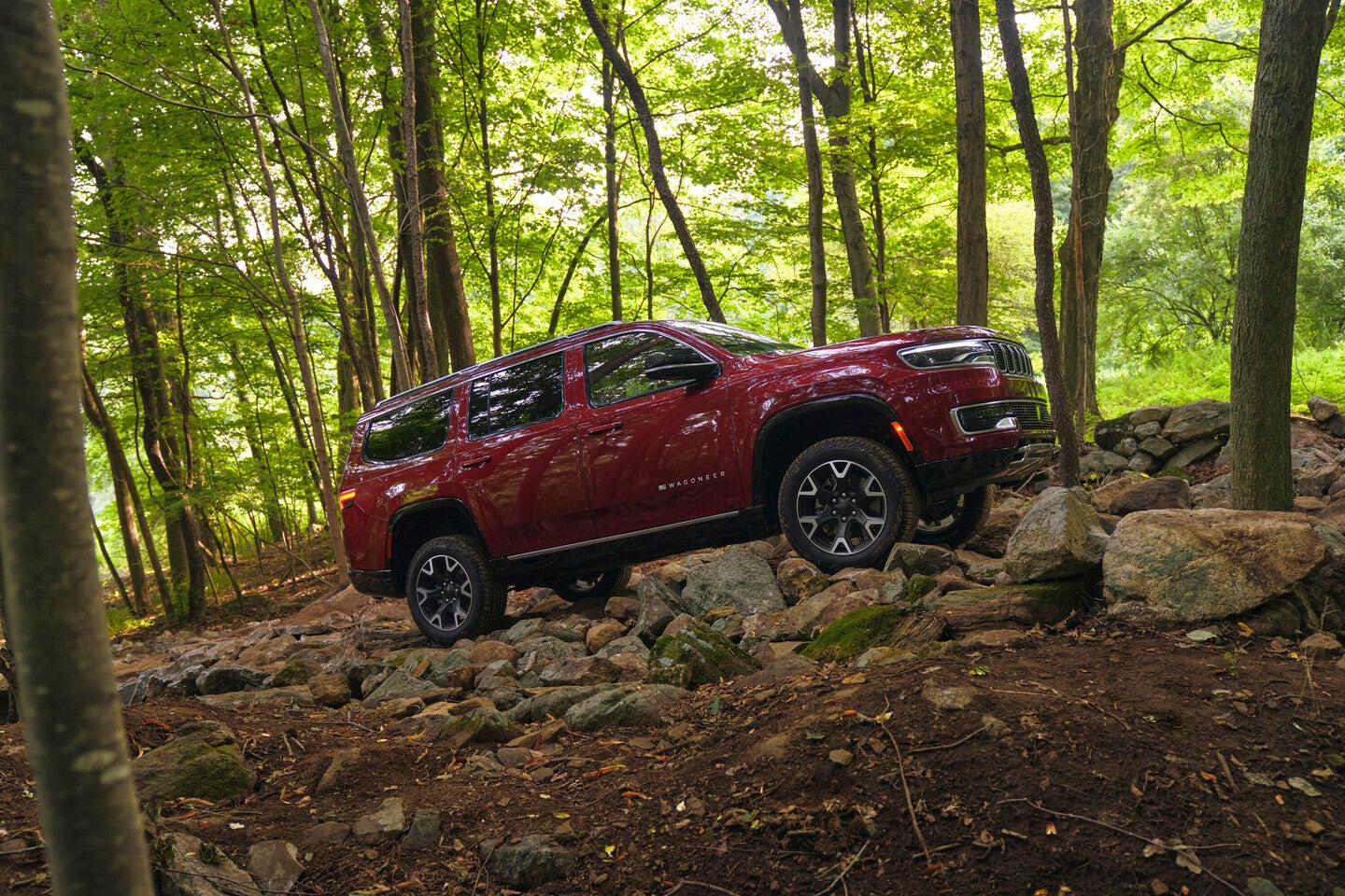 a dark red 2025 jeep wagoneer driving through rocky terrain in the woods