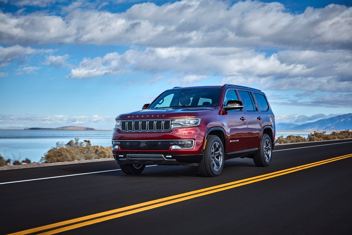 a dark red 2025 jeep wagoneer driving on a highway next to water