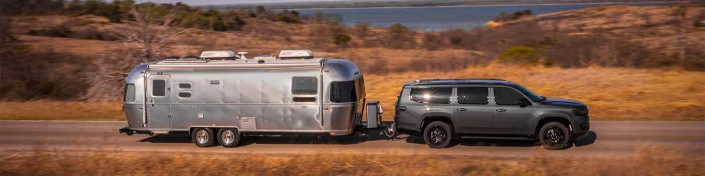 2025 jeep wagoneer hauling a silver bullet camper with desert terrain in the background