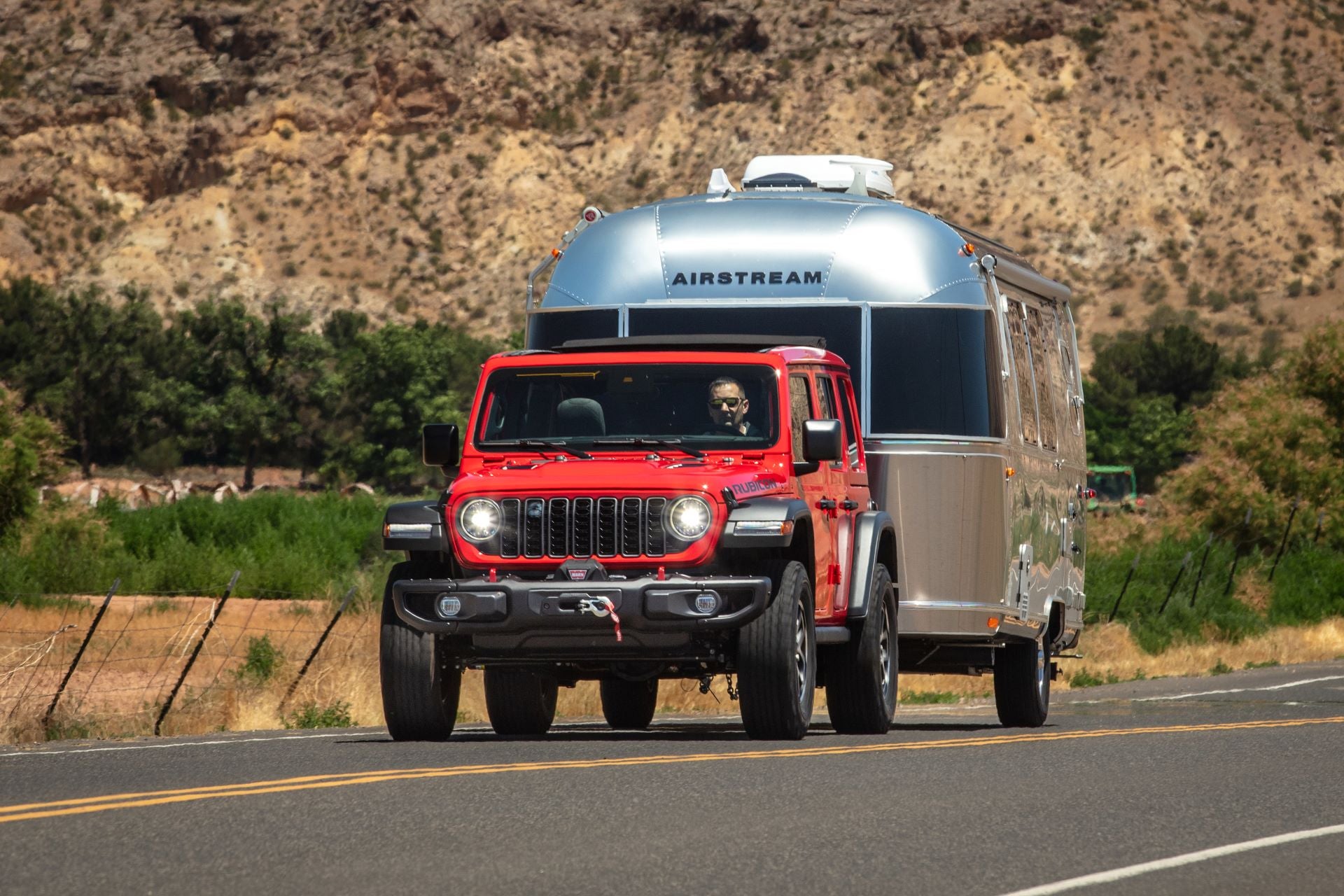 the front of a red jeep wrangler towing a silver bullet camper