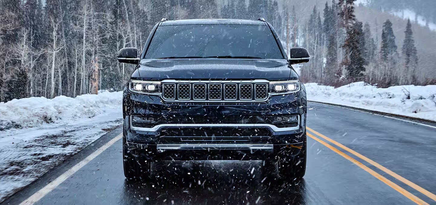 The front grille of a black 2025 Jeep Grand Wagoneer on a snowy road.