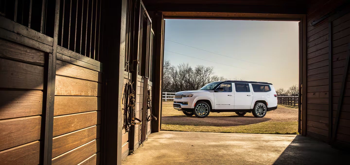 A white 2025 Jeep Grand Wagoneer photo shot through a barn during sunset.