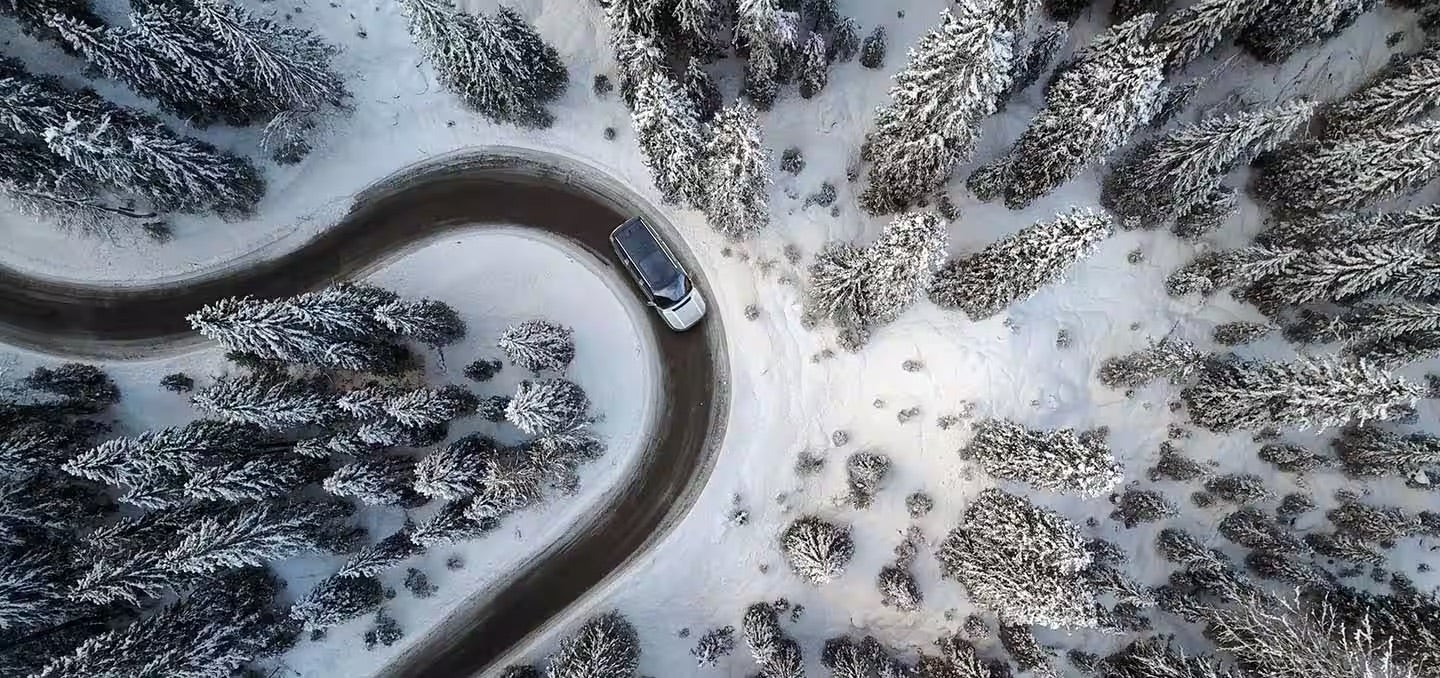 An aerial image of a 2025 white Jeep Grand Wagoneer driving on a snowy road.