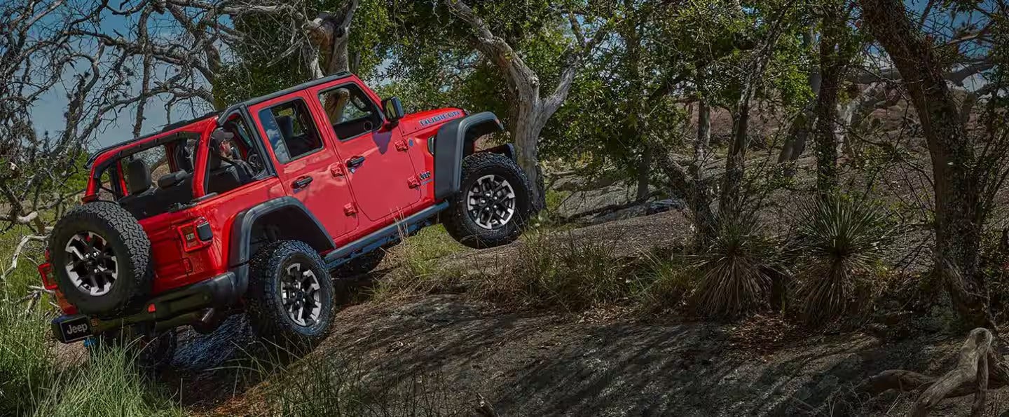 A red car jeep driving up a hill.