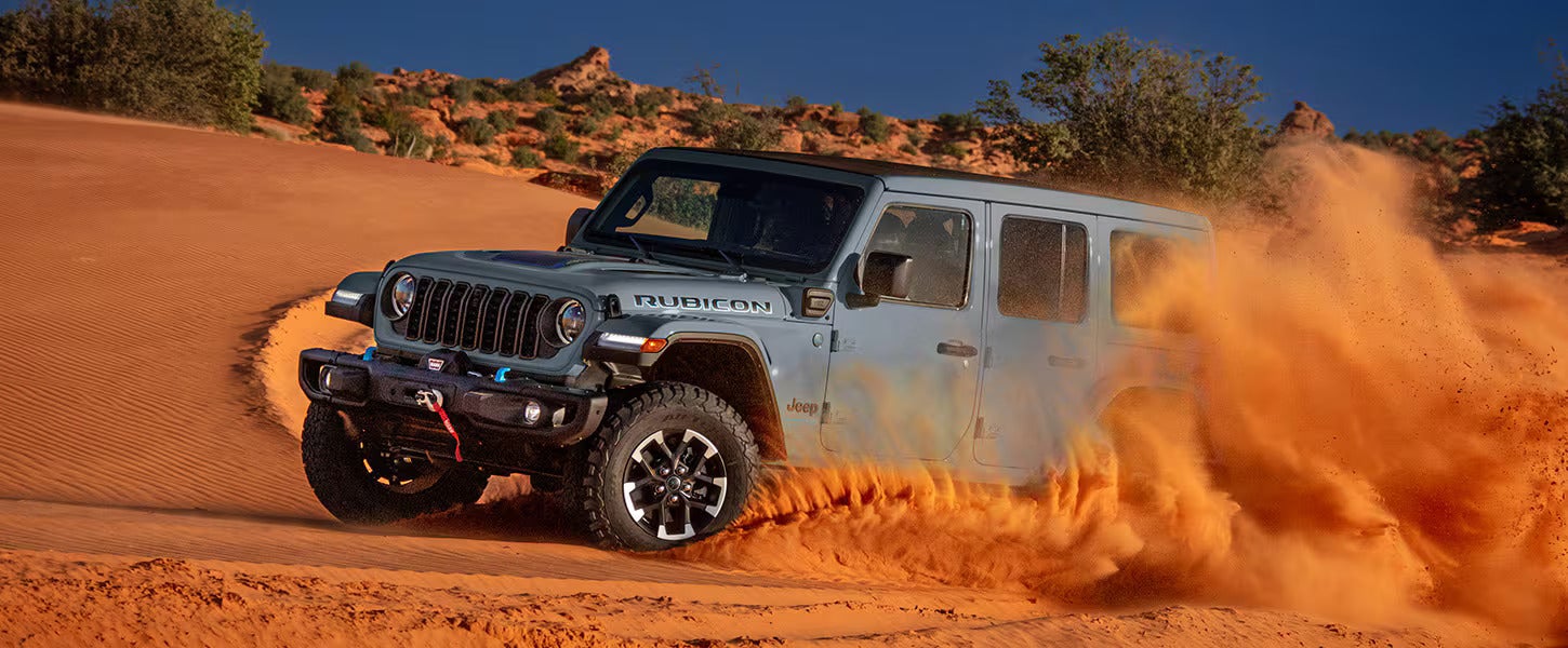A gray jeep driving through the sand.