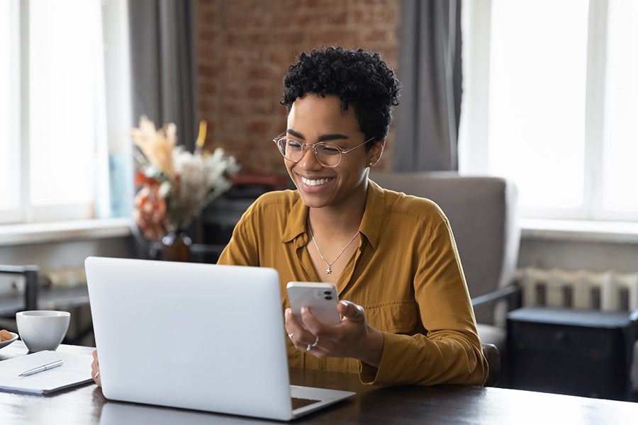 a woman looking at her computer and a phone at home